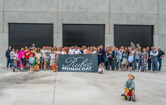 Group photo of Rubio Monocoat's employees in front of the building with a flag with the Rubio Monocoat logo on