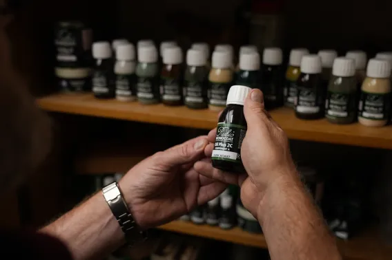 Someone is holding a small bottle of wood oil in their hands in front of a row of bottles in a cabinet