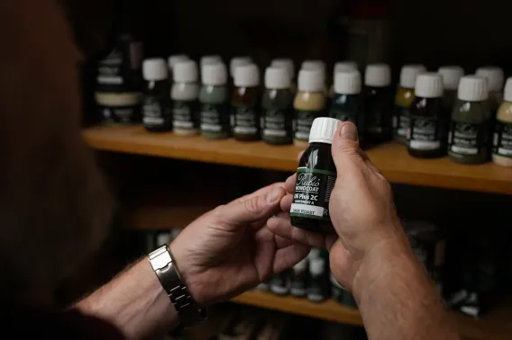 Someone is holding a bottle of wood oil in his hands in front of a cabinet with all colours lined up