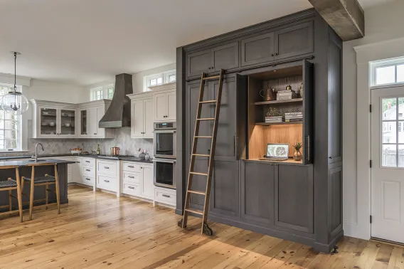 A country kitchen with lots of wooden cabinets, a wooden ladder and a wooden floor