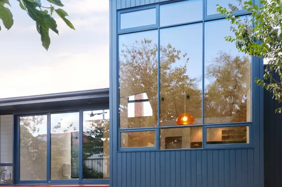 A modern house is shown with lots of glass windows and a blue wooden cladding