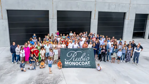 The employees are gathered outside the plant holding a flag of Rubio Monocoat