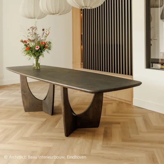 A dark wooden table in special design stands on top of a natural herringbone wooden floor and in front of dark wooden slats