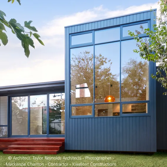 A modern house is shown with lots of glass windows and a blue wooden cladding