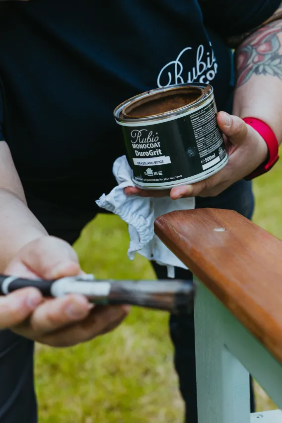 A hand applying DuroGrit with a brush on a detail of a bench