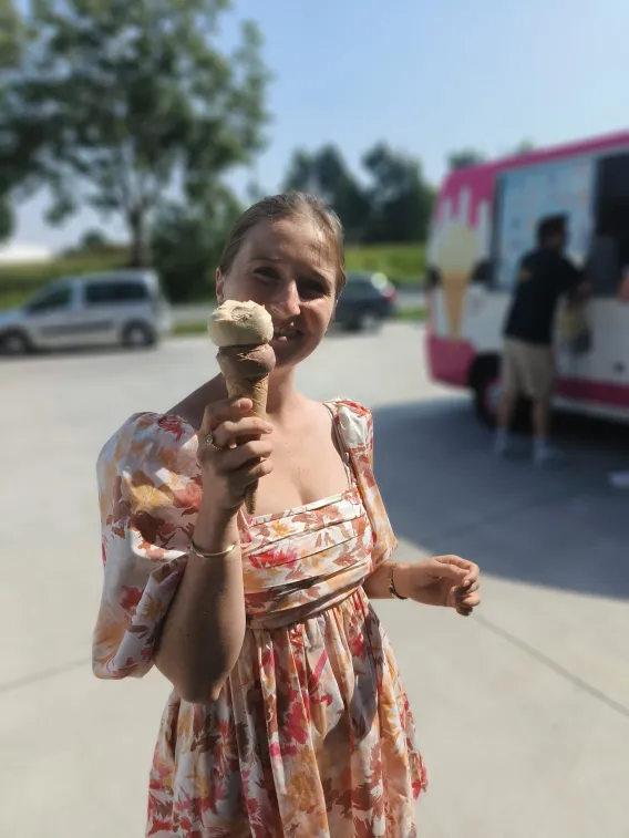An employee is smiling with an ice cream in hand. The ice cream truck is behind her.